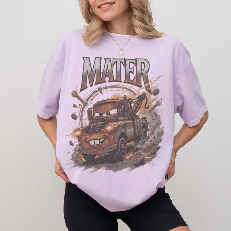 Puede incluir: Camiseta lila claro con una imagen de dibujos animados de Mate de la pel&iacute;cula Cars. El gr&aacute;fico incluye el nombre "MATER" en una fuente desgastada sobre el cami&oacute;n. El dise&ntilde;o tiene un aspecto vintage y desgastado.