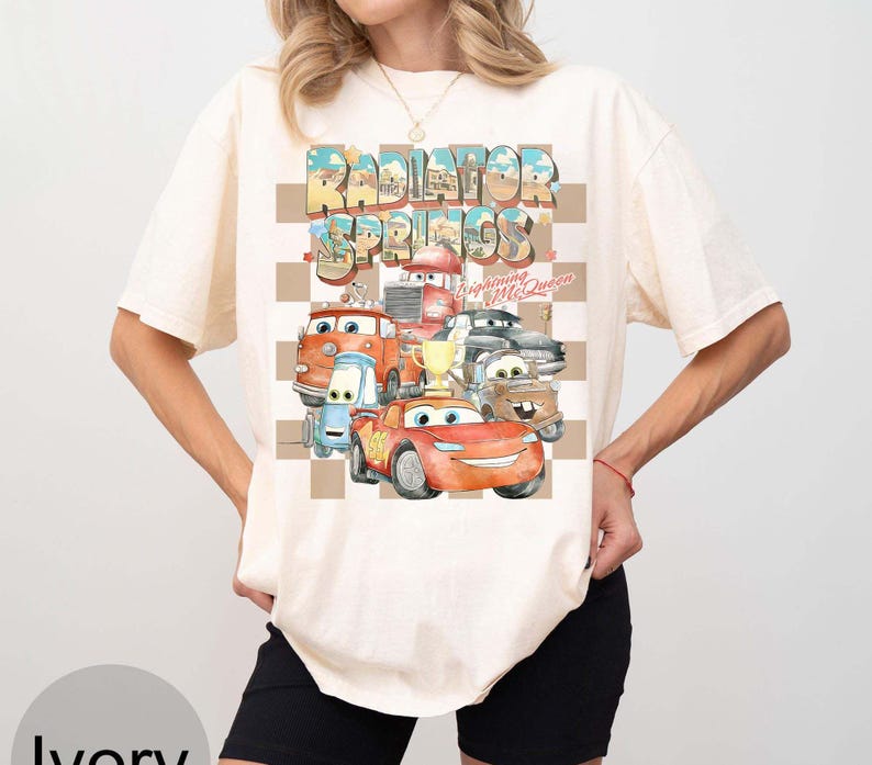 Peut inclure: T-shirt ivoire avec un motif color&eacute; de personnages du film Cars, dont Flash McQueen, et le texte "Radiator Springs". Le motif est plac&eacute; sur un fond &agrave; carreaux.