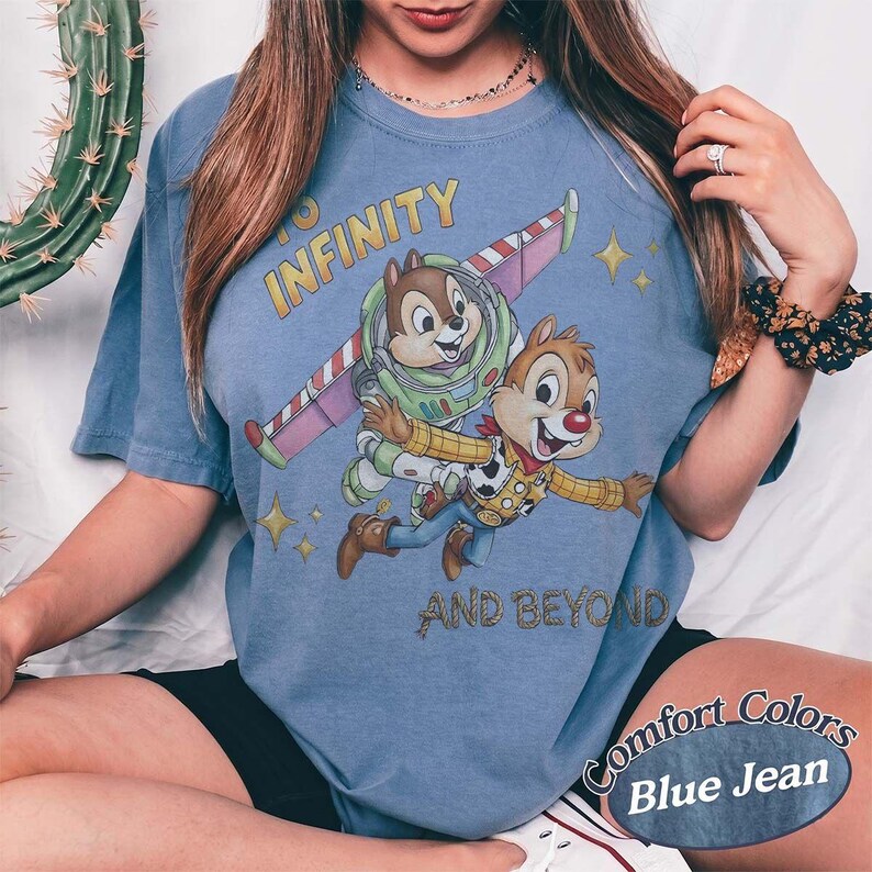 Puede incluir: Camiseta azul vaquero con Chip y Dale como Buzz Lightyear y Woody, con el texto "To Infinity and Beyond". La camiseta tiene un aspecto desgastado y las palabras "Comfort Colors" est&aacute;n impresas en la parte inferior.