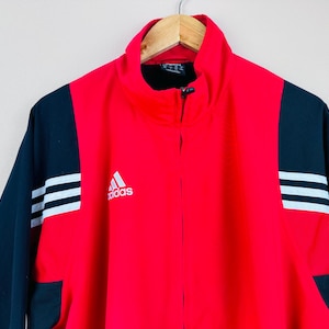 May include: Red and black Adidas track jacket with white stripes and the Adidas logo on the front.