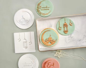 May include: A set of five cookie cutters with Islamic designs. The cutters are made of white plastic and feature a crescent moon, a mosque, a lantern, and the words "Ramadan Mubarak" and "Eid Mubarak".