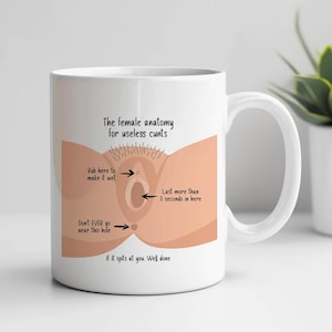 以下が含まれることがあります： ユーモラスな女性の解剖図と「The female anatomy for useless cunts」というテキストが描かれた白いセラミックマグ。マグには、「Rub here to make it wet」や「Last more than 3 seconds in here」などの指示やフレーズも含まれています。