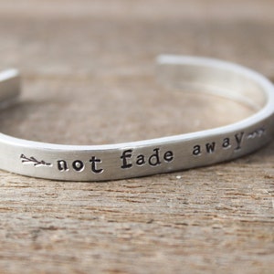 May include: Silver bracelet with the inscription "not fade away" and a small arrow design.