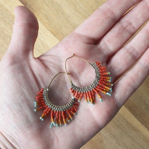 May include: A pair of hoop earrings with a fringe of orange, gray, and turquoise beads.
