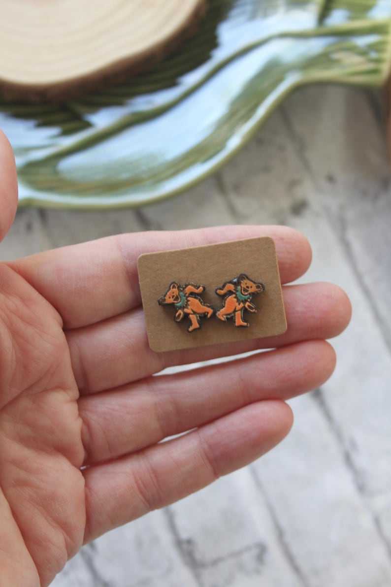 May include: A pair of brown wooden earrings with a design of two dancing bears. The earrings are on a small brown card.