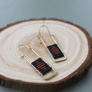 May include: A pair of gold hoop earrings with a black and brown beaded design. The beads are arranged in a geometric pattern.