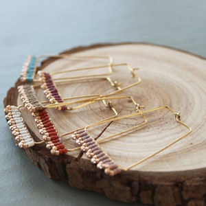 May include: Four pairs of gold hoop earrings with beaded accents. The beads are in various colors, including white, red, brown, and blue.
