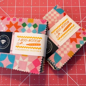 May include: Two stacks of pink fabric squares with colorful geometric patterns, including orange stars, teal shapes, and green squares. Each stack is wrapped with a label that reads "1-800-NOTION" and "Collaborative Collection". The squares are 2.5 inches.