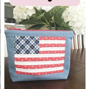 May include: A denim pouch with a sewn American flag design. The flag features a blue and white plaid pattern for the stars and red and white stripes. The pouch is approximately 9 inches by 10 inches.