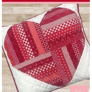 May include: A heart-shaped pillow with a patchwork design in various shades of red and white. The pillow is quilted and has a white border. The text "Twisted Heart Pillow Pattern" is visible.