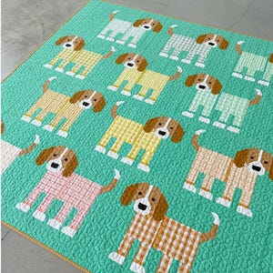 May include: A quilt featuring a repeating pattern of stylized dogs on a bright teal background. Each dog has a brown head and a body made of gingham fabric in various pastel colors including yellow, pink, and light green, with white paws.