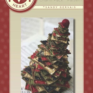 May include: A Tiny Tree Charm Pack pattern by Sandy Gervais. The image shows a small, handmade Christmas tree made from layered fabric squares in red, green, and beige. The tree sits on sheet music.
