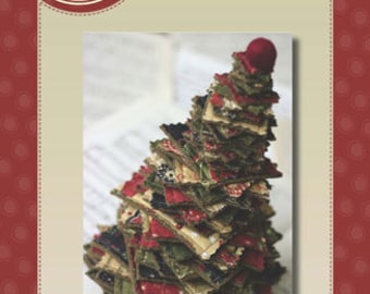 May include: A Tiny Tree Charm Pack pattern by Sandy Gervais. The image shows a small, handmade Christmas tree made from layered fabric squares in red, green, and beige. The tree sits on sheet music.