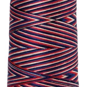 May include: A spool of Mettler SILK-FIN Cotton mercerized thread, featuring a vibrant pattern of red, white, and navy blue diagonal stripes. The spool has a light purple base and top with the brand name printed on the top.