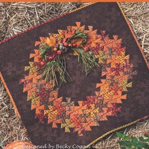 May include: A square, brown quilt with a fall-themed wreath design. The wreath is made of orange, yellow, and red fabric pieces. The text "Twister Harvest" is at the top, and "Real Love" is at the bottom.