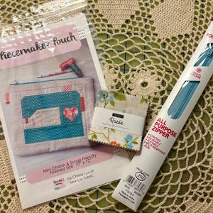 May include: A sewing-themed craft kit with a pouch pattern, fabric samples, and a blue zipper. The pouch pattern features a sewing machine design with a heart. The zipper is 12 inches (30 cm) long.