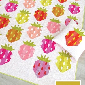 May include: A white quilt and pillow set with a repeating pattern of colorful, geometric strawberries. The strawberries are in shades of red, pink, orange, and yellow. The text "BERRY SEASON" is displayed above the quilt. The pattern is by Elizabeth Hartman.