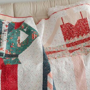 May include: Two handmade quilts with festive designs. One quilt features a green and red elf costume design, while the other showcases a red dress pattern. Both quilts are on a white background with a dotted pattern.