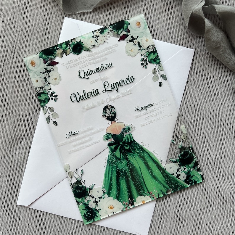 Op de afbeelding: Een transparante acryl Quincea&ntilde;era-uitnodiging met een groen en wit bloemenontwerp. De uitnodiging toont een tekening van een meisje in een groene jurk met een witte strik. De tekst op de uitnodiging luidt "El Se&ntilde;or y la Se&ntilde;ora los invitan a celebrar Quincea&ntilde;era de su hija Valeria Lupercio".