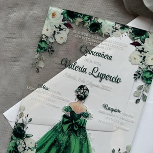 Op de afbeelding: Een uitnodiging voor een Quincea&ntilde;era met een groen en wit bloemenontwerp. De uitnodiging toont een groene jurk met een witte strik en een bloemenkroon. De tekst op de uitnodiging luidt "Quincea&ntilde;era de su hija Valeria Lupercio, S&aacute;bado, 6 de Agosto 2022".