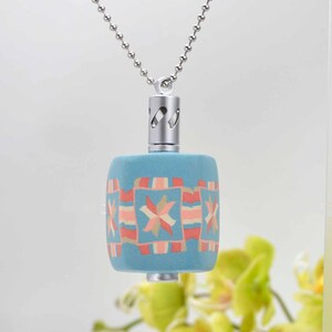 May include: A blue and pink patterned ceramic pendant on a silver chain. The pendant has a geometric design with a star in the center. The pendant is attached to a silver chain with a silver cap.