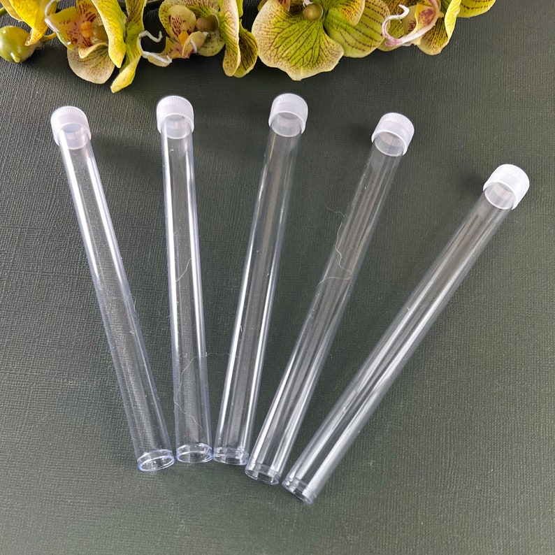 May include: Five clear plastic tubes with white lids. The tubes are arranged in a fan shape on a dark green surface.