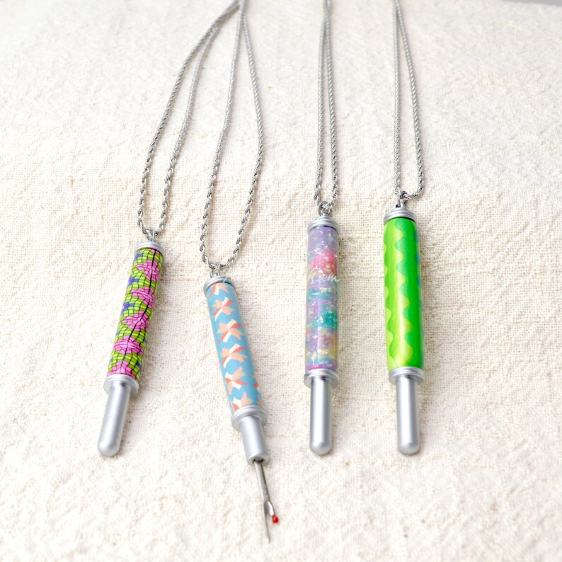 Peut inclure: Quatre colliers avec des d&eacute;coud-vite et des cha&icirc;nes argent&eacute;es. Les d&eacute;coud-vite pr&eacute;sentent des motifs color&eacute;s : un motif g&eacute;om&eacute;trique rose et vert, un motif crois&eacute; bleu et p&ecirc;che, un motif de confettis scintillants et un motif vert ondul&eacute;. Les d&eacute;coud-vite sont argent&eacute;s.