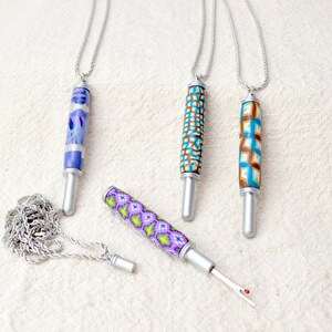 May include: Four decorative seam rippers with silver-colored metal components and colorful polymer clay handles. The handles feature various patterns in blue, purple, green, and brown. One ripper is detached, revealing the blade. Each ripper is attached to a silver chain.