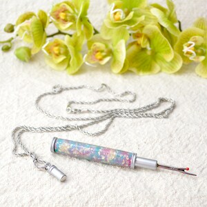 Peut inclure: Un d&eacute;couseur argent&eacute; avec un manche tubulaire iris&eacute; d&eacute;coratif et une cha&icirc;ne assortie. La poign&eacute;e pr&eacute;sente un motif tachet&eacute; color&eacute; dans les tons rose, bleu et or. La lame du d&eacute;couseur a une pointe rouge.