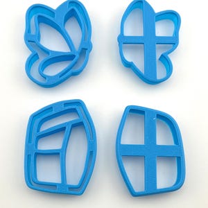 May include: Four blue plastic cookie cutters in various shapes. The shapes include a butterfly, a bow, and two abstract designs. The cutters are made of a solid, bright blue plastic and are set against a white background.