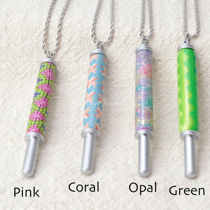 Peut inclure: Quatre colliers avec pendentifs cylindriques. Chaque pendentif a une base et un sommet argent&eacute;s, suspendus &agrave; une cha&icirc;ne argent&eacute;e. Les pendentifs sont &eacute;tiquet&eacute;s "Pink", "Coral", "Opal" et "Green". Le pendentif rose a un motif mosa&iuml;que.