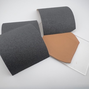 May include: An assortment of sanding pads and a small, clear, rectangular piece of glass. The sanding pads are black with a textured surface. A brown, geometric-shaped piece is also present.
