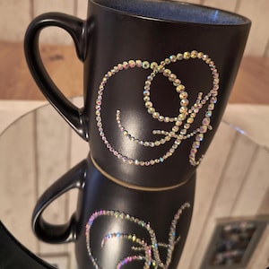 May include: Black ceramic mug with a decorative design of a swirl made of iridescent rhinestones.