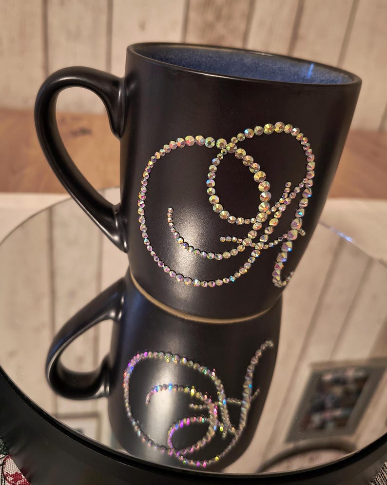 May include: Black ceramic mug with a decorative design of a swirl made of iridescent rhinestones.