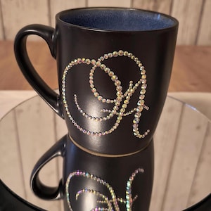 May include: Black ceramic mug with a sparkly iridescent design of the letter "A" on the side.