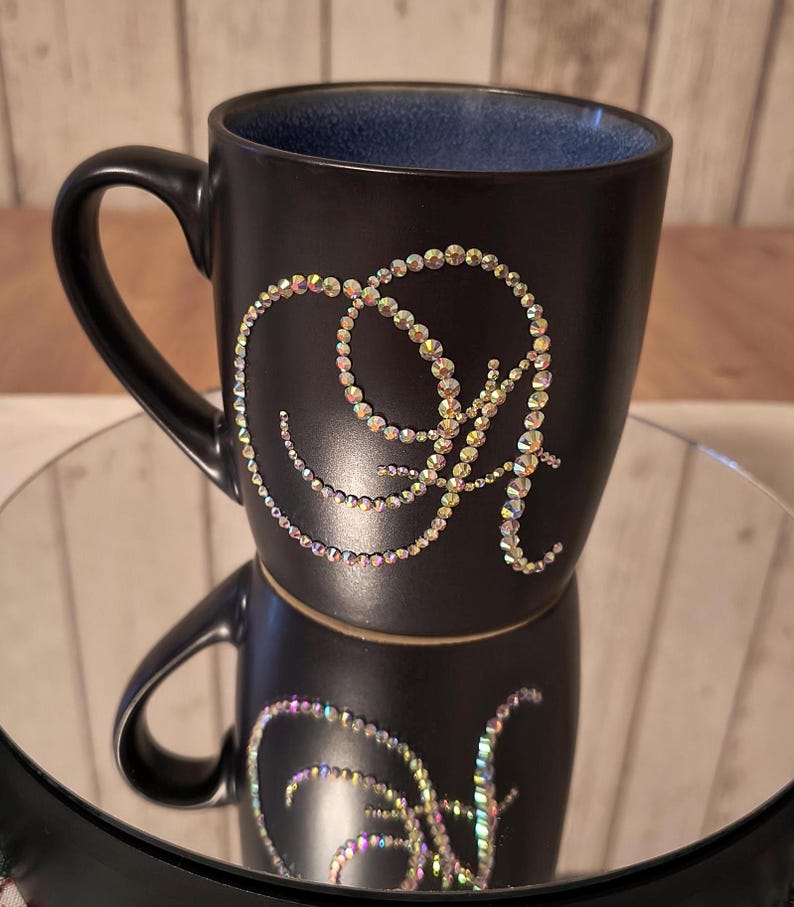 May include: Black ceramic mug with a sparkly iridescent design of the letter "A" on the side.