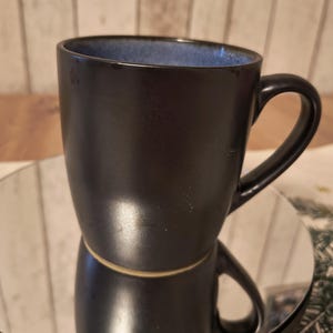 May include: A black ceramic mug with a blue rim and a handle. The mug has a glossy finish.