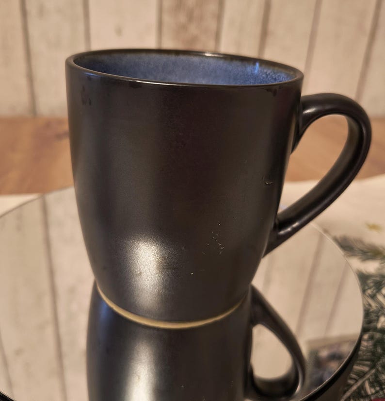 May include: A black ceramic mug with a blue rim and a handle. The mug has a glossy finish.