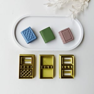 Puede incluir: Tres pequeños moldes de silicona en forma de libro en azul, verde y rosa, y tres moldes de silicona en forma de libro más grandes en amarillo.