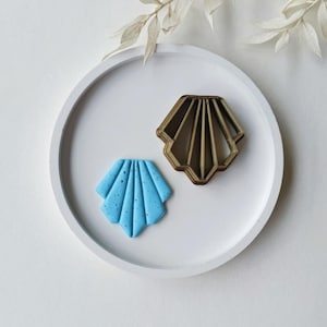 May include: A blue and white shell-shaped cookie cutter and a blue shell-shaped cookie on a white plate.