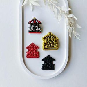 Könnte beinhalten: Vier Karussell-Ausstecher, einer rot, einer schwarz, einer goldfarben und einer mit roten, weißen und schwarzen Details. Die Ausstecher befinden sich auf einem weißen ovalen Tablett.