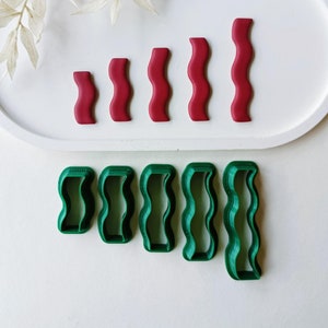 Könnte beinhalten: Fünf rote und fünf grüne Plastik-Ausstecher in Form von Wellenlinien. Die Ausstecher sind in zwei Reihen auf einer weißen Oberfläche angeordnet.