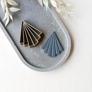 May include: Two geometric shapes, one gold and one blue, on a grey concrete tray. The shapes are both fan-shaped and have a pointed top.