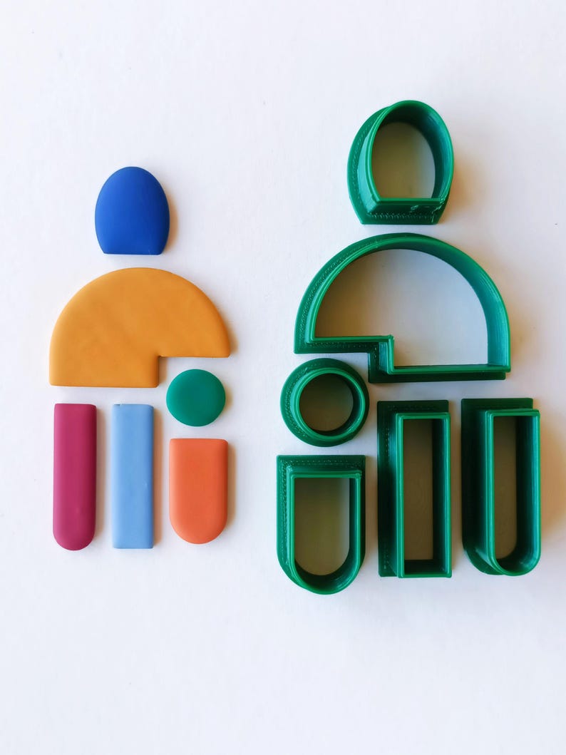 May include: A set of green plastic cookie cutters in various shapes, including a large arch, a circle, a rectangle, and a smaller arch. There are also several small pieces of colorful clay in different shapes.