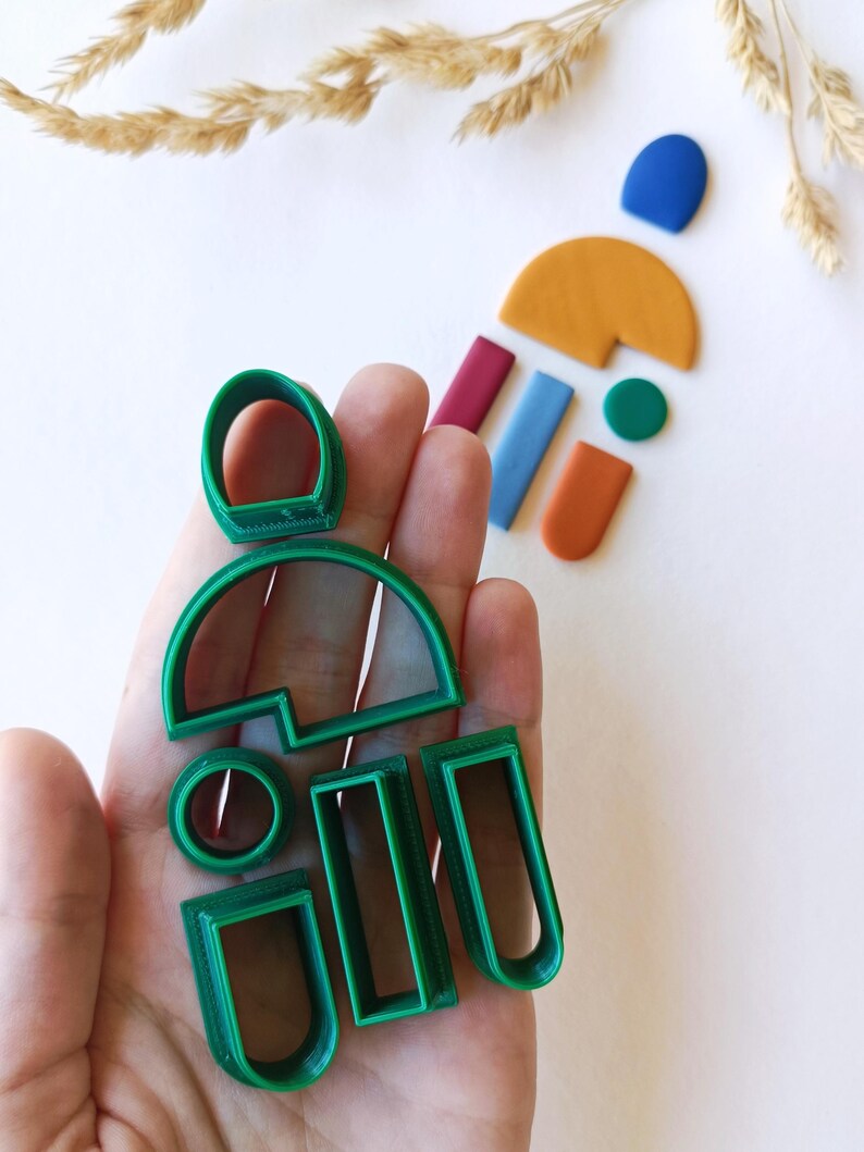 May include: A set of green plastic cookie cutters in various shapes, including circles, rectangles, and arches. The cutters are held in a hand.