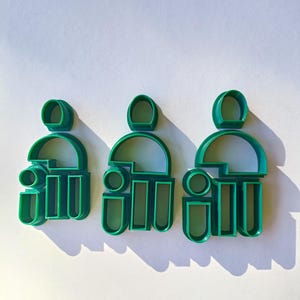 May include: Three green plastic cookie cutters shaped like people. Each cutter has a head, torso, and legs.