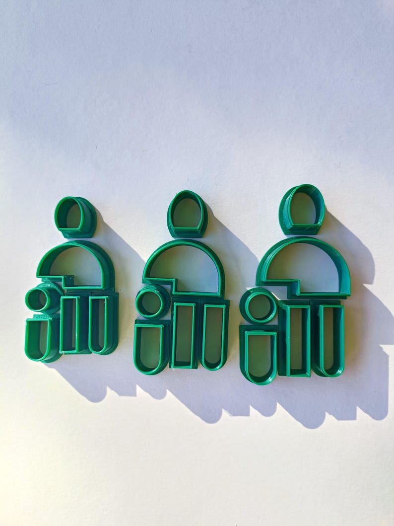 May include: Three green plastic cookie cutters shaped like people. Each cutter has a head, torso, and legs.