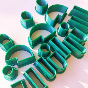 May include: A set of 14 green plastic cookie cutters in various shapes, including circles, squares, rectangles, and arches.