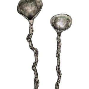 May include: Two silver serving spoons with unique, textured, branch-like handles. The spoons have a rounded, shell-like bowl.