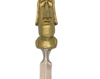 May include: A letter opener featuring a gold-colored handle shaped like a stylized Moai statue head with a textured surface. The handle is attached to a smooth, silver-colored metal blade that tapers to a point, creating a functional office tool.